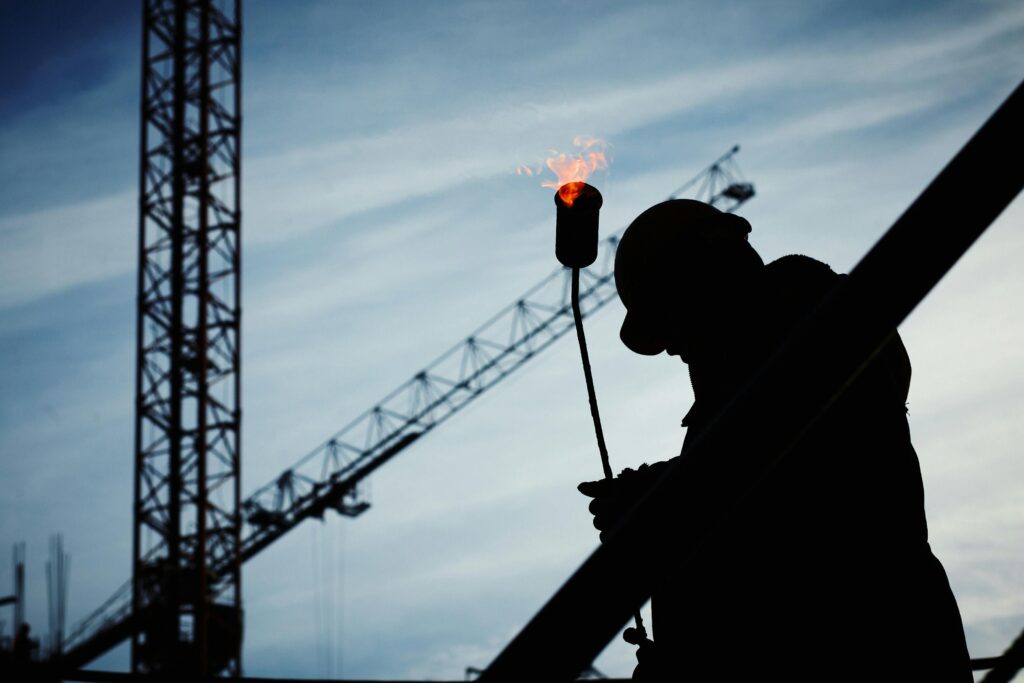 pexels-photo-585418-585418 Silhouette of a construction worker using a blowtorch at a building site against a crane-filled skyline.