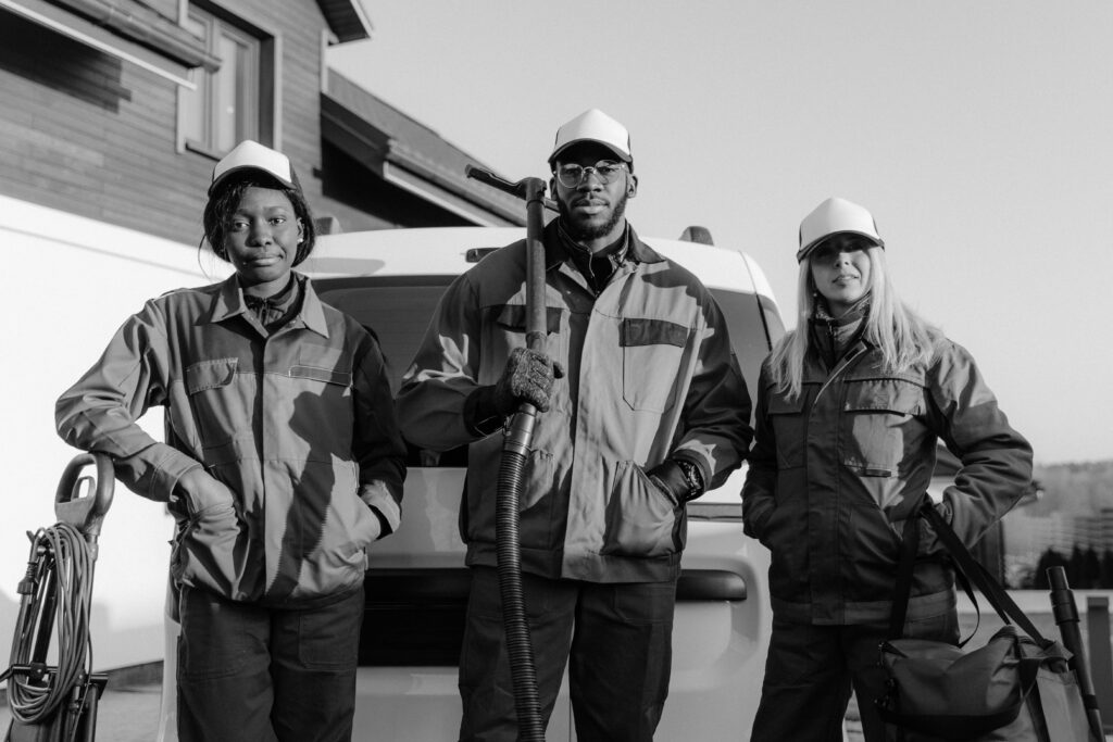 pexels-photo-6196225-6196225 Three professional cleaners in uniform pose with equipment in front of a building.